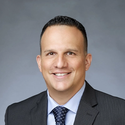 a headshot of chirorpactor Dr. James wearing a dark gray business suit, light blue dress shirt, and navy patterned tie.